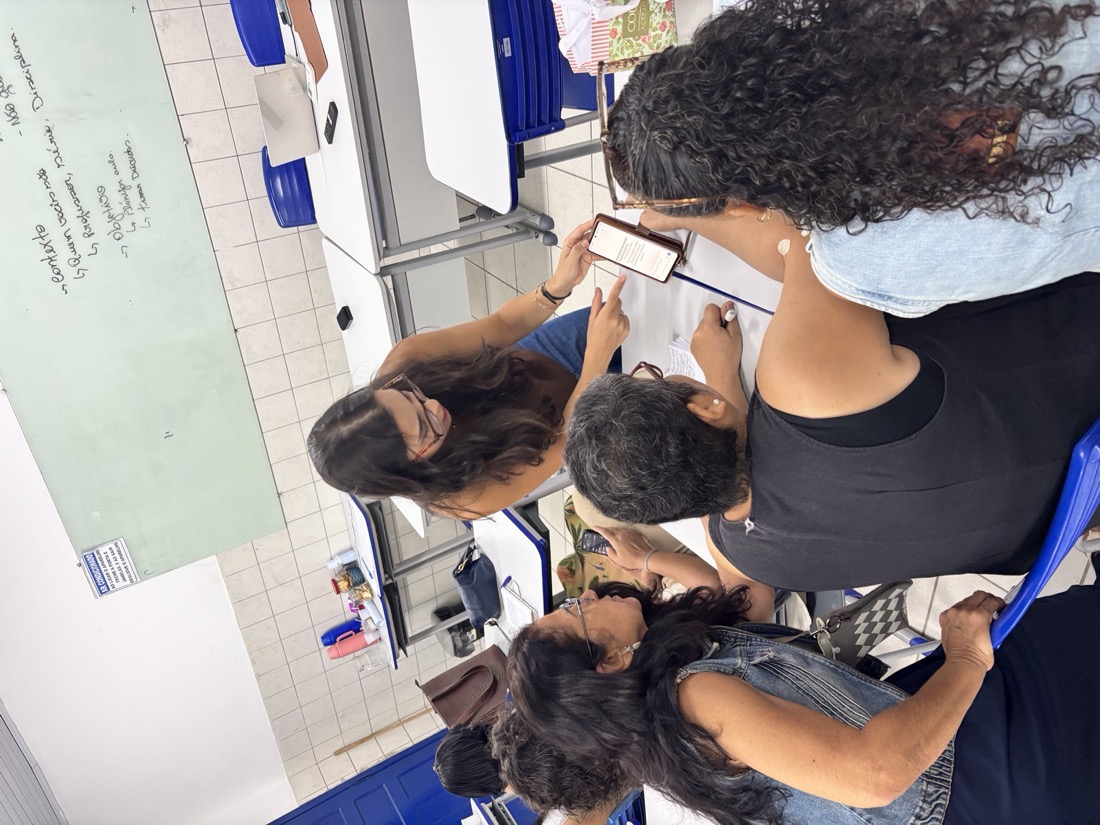 Raquel Galvão em atendimento próximo, mostrando o celular pra um grupo de professoras durante a atividade prática